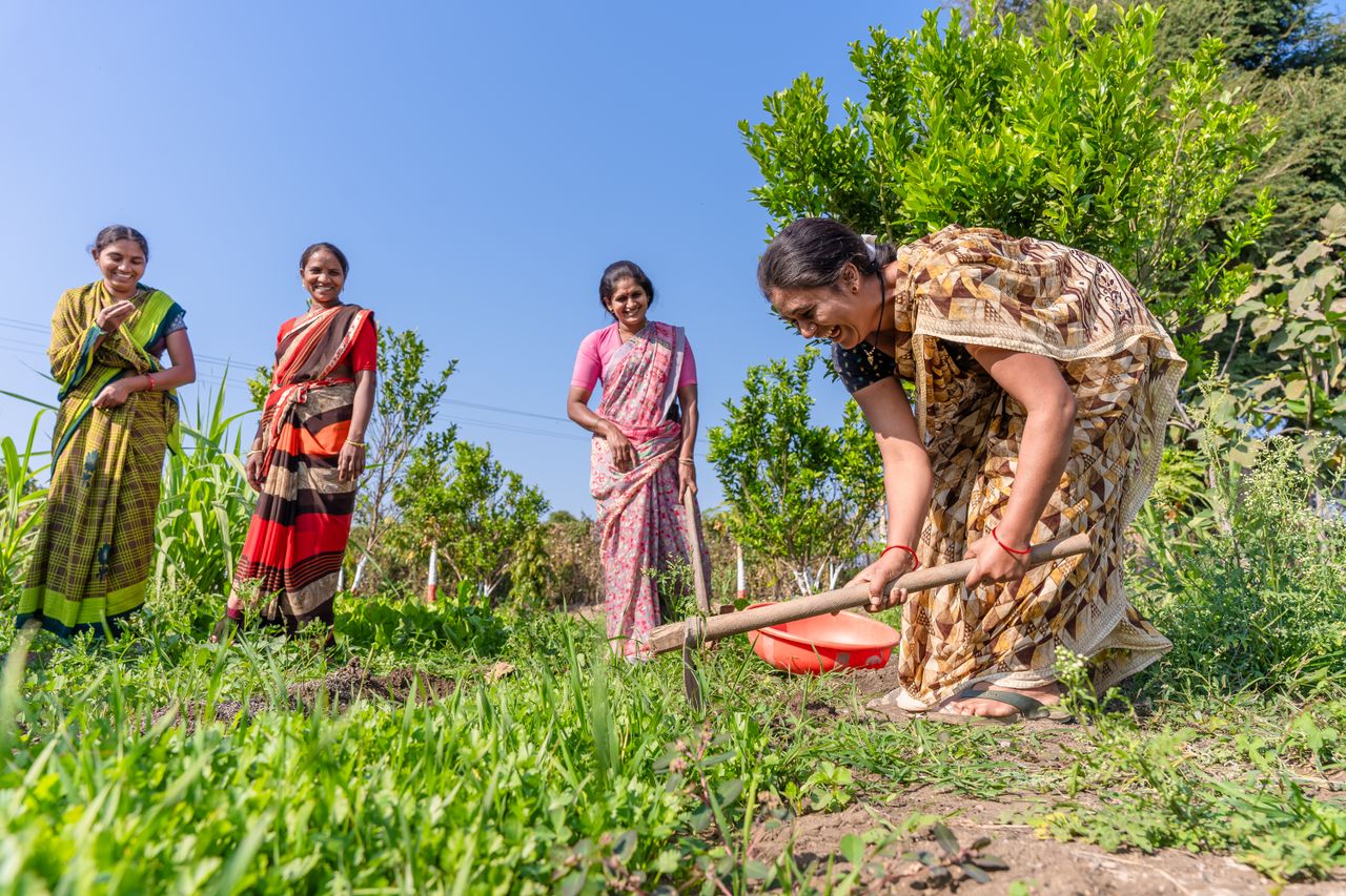 Group of Indian women farmers working joyfully in a lush green field under a clear blue sky.